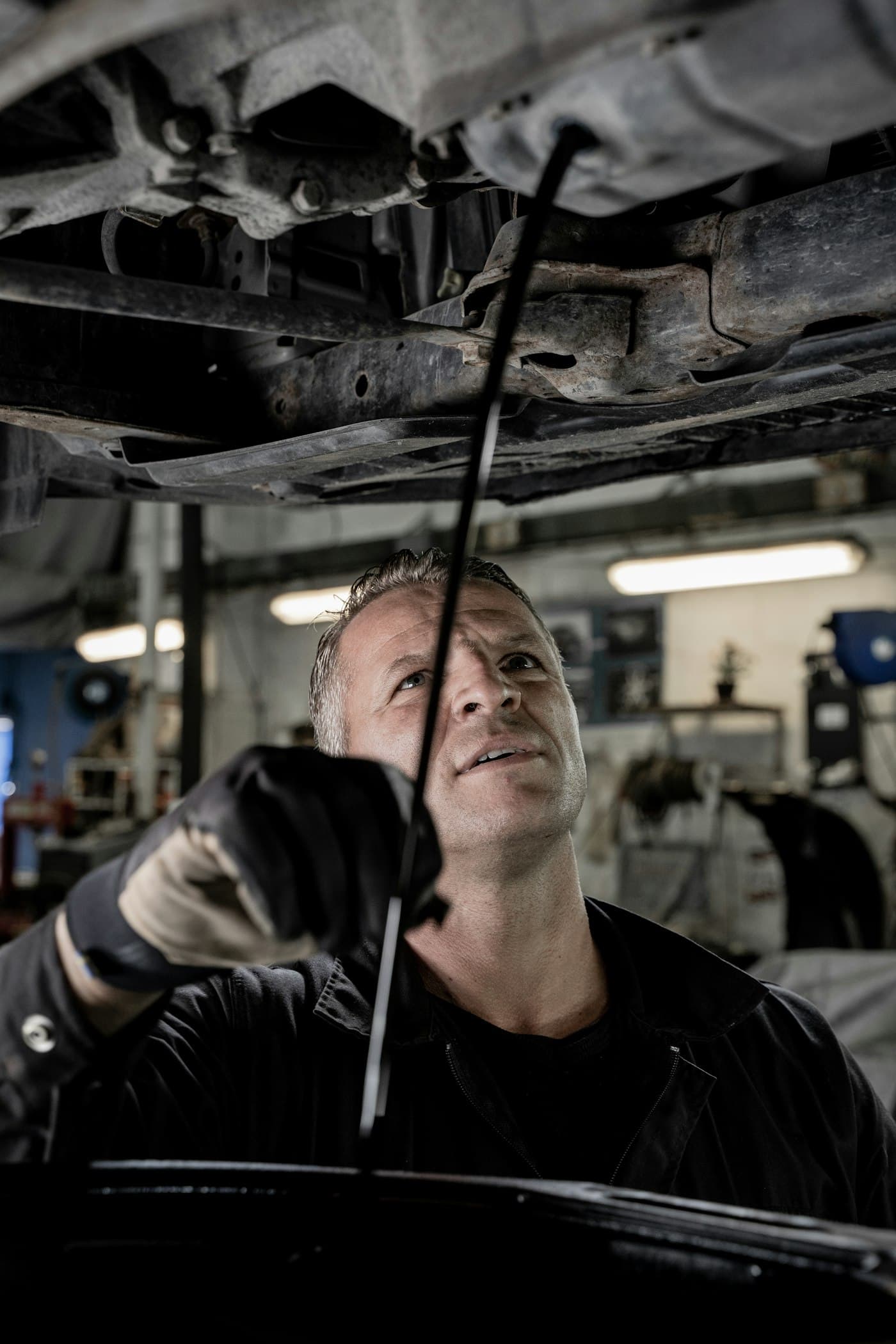 A mechanic looking up while working under a vehicle in a garage