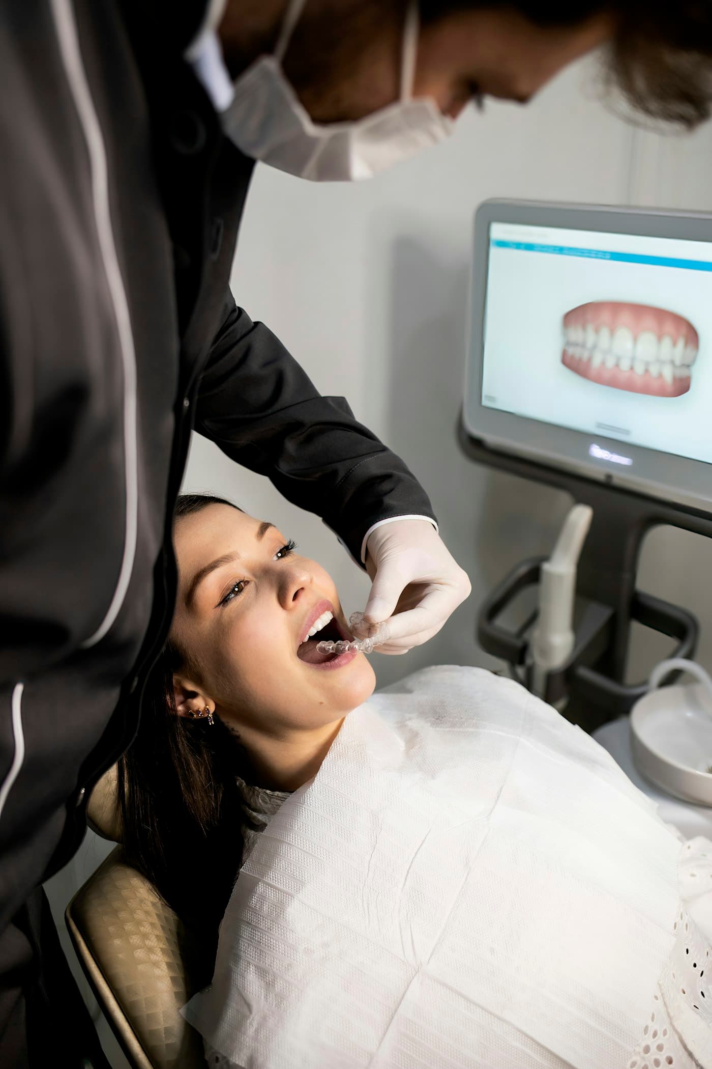 A dental patient smiling in the chair while a clinician shows an aligner